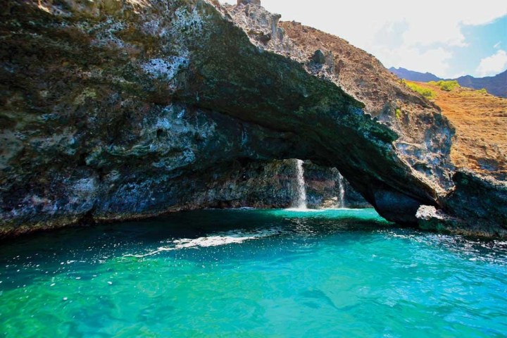 Sea Arch with waterfalls behind them on the north coast of Kauai