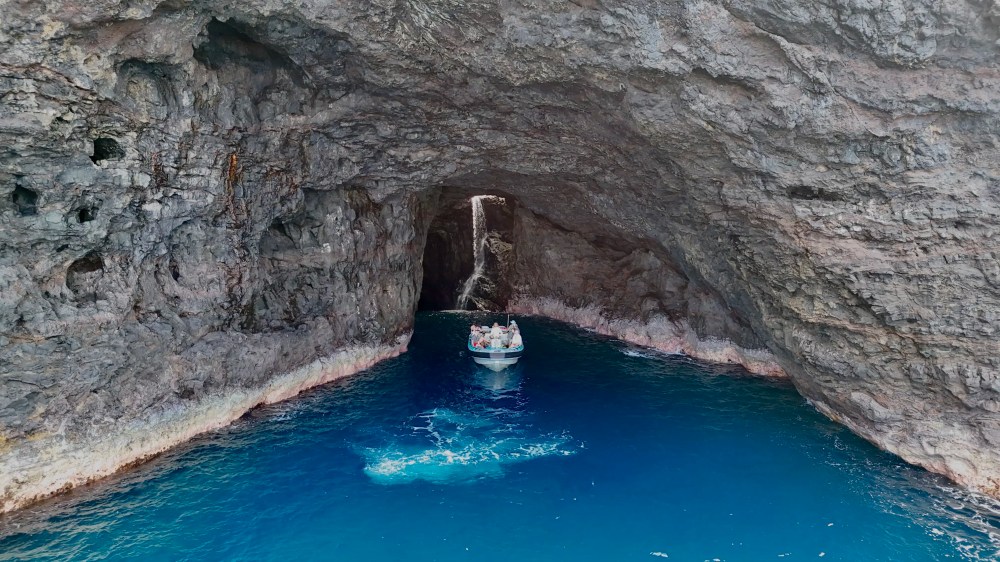 Boat under a rocky arch in a sea cave with deep blue water.