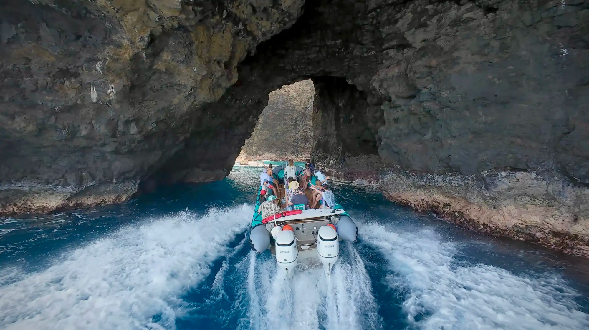 Boat with people entering a rocky sea cave on blue water.