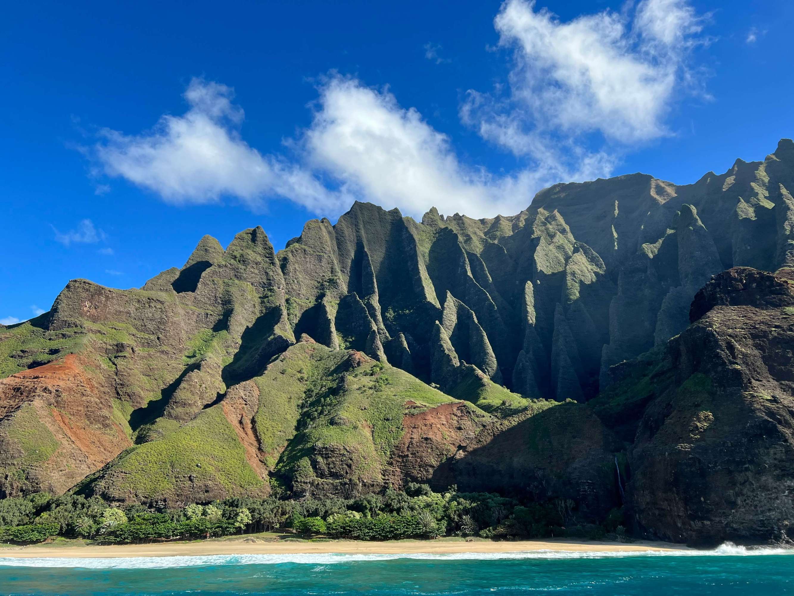 a view of the cliffs of the na pali coast from a boat in the water with the clear blue sky in the background