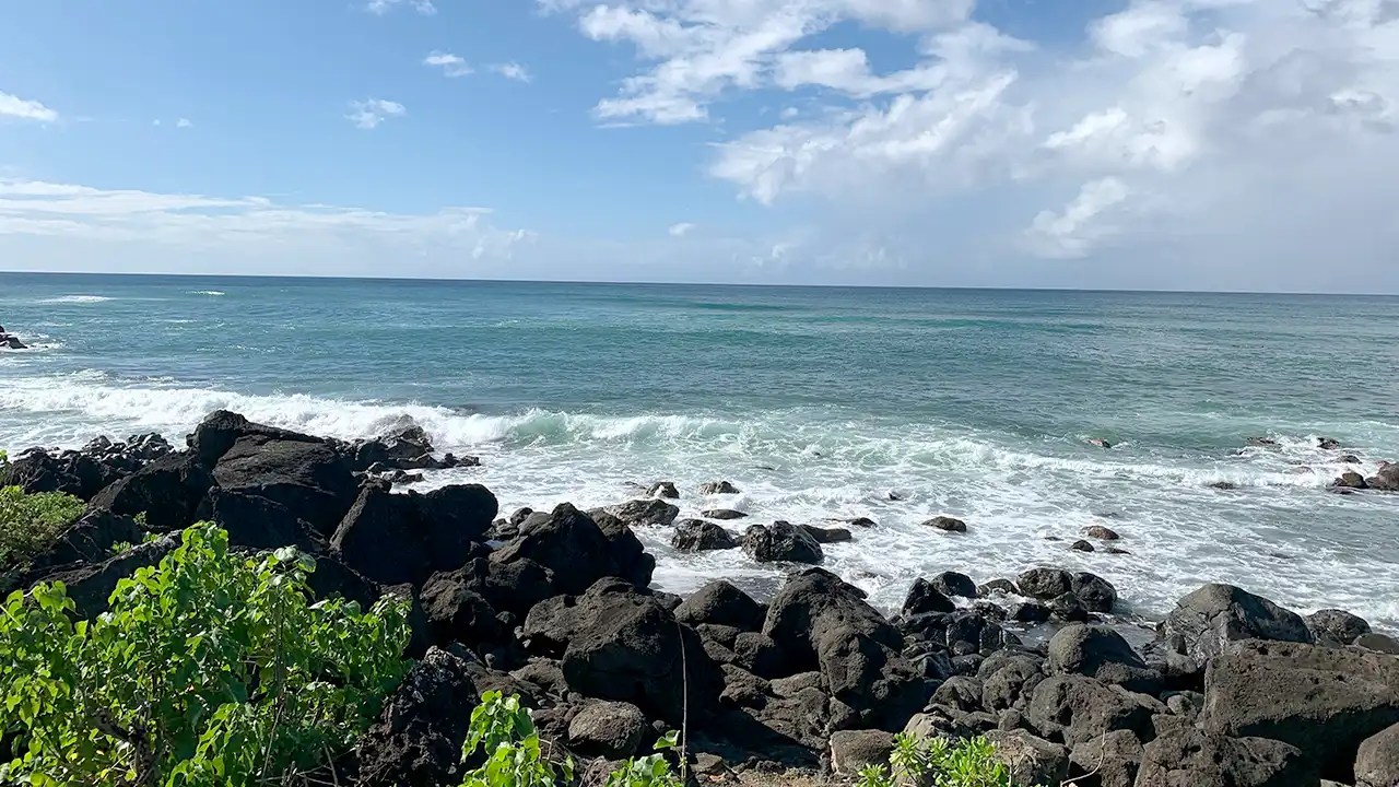 anini-beach-kauai_family-friendly-beach Rocky shoreline with waves under a partly cloudy sky.