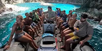 People sitting in a boat on turquoise water, surrounded by rocky cliffs.