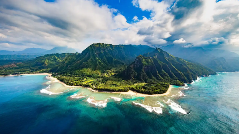 Aerial view of a lush, mountainous coastline with blue ocean and white waves.