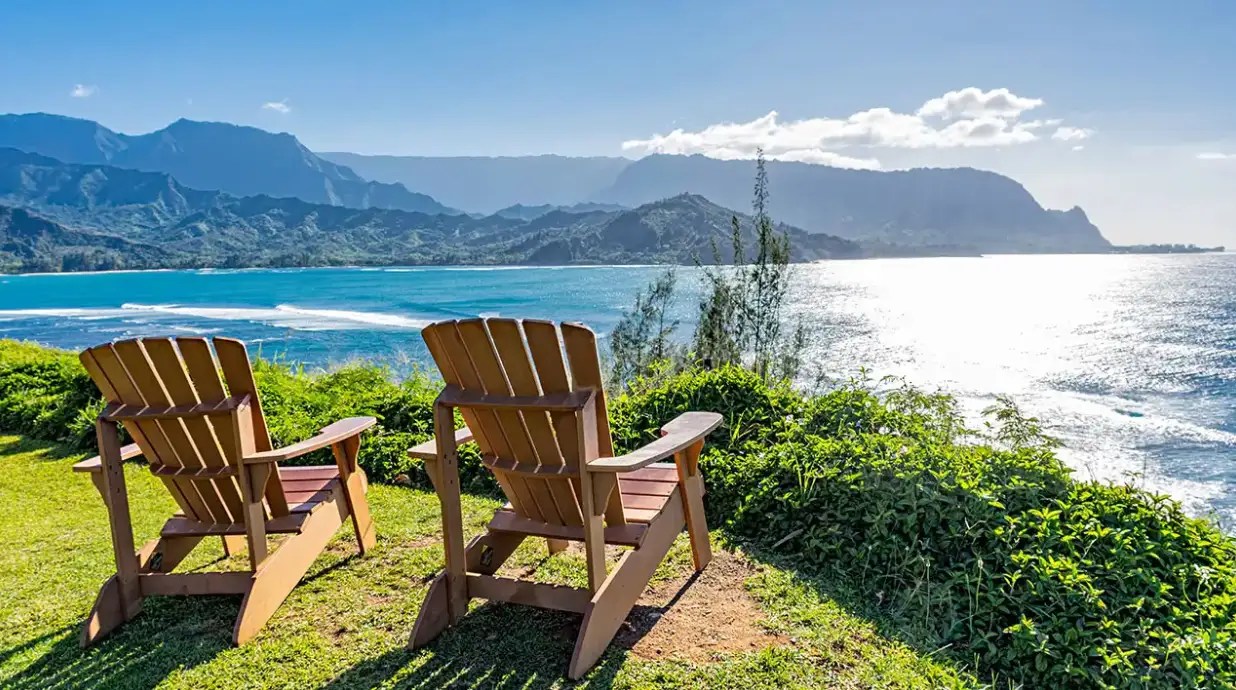 Two chairs overlooking an ocean view with mountains and blue sky.