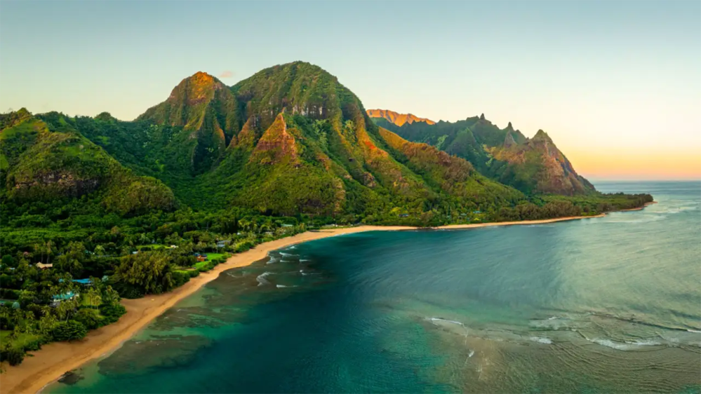 Scenic view of a beach with lush green mountains at sunset.