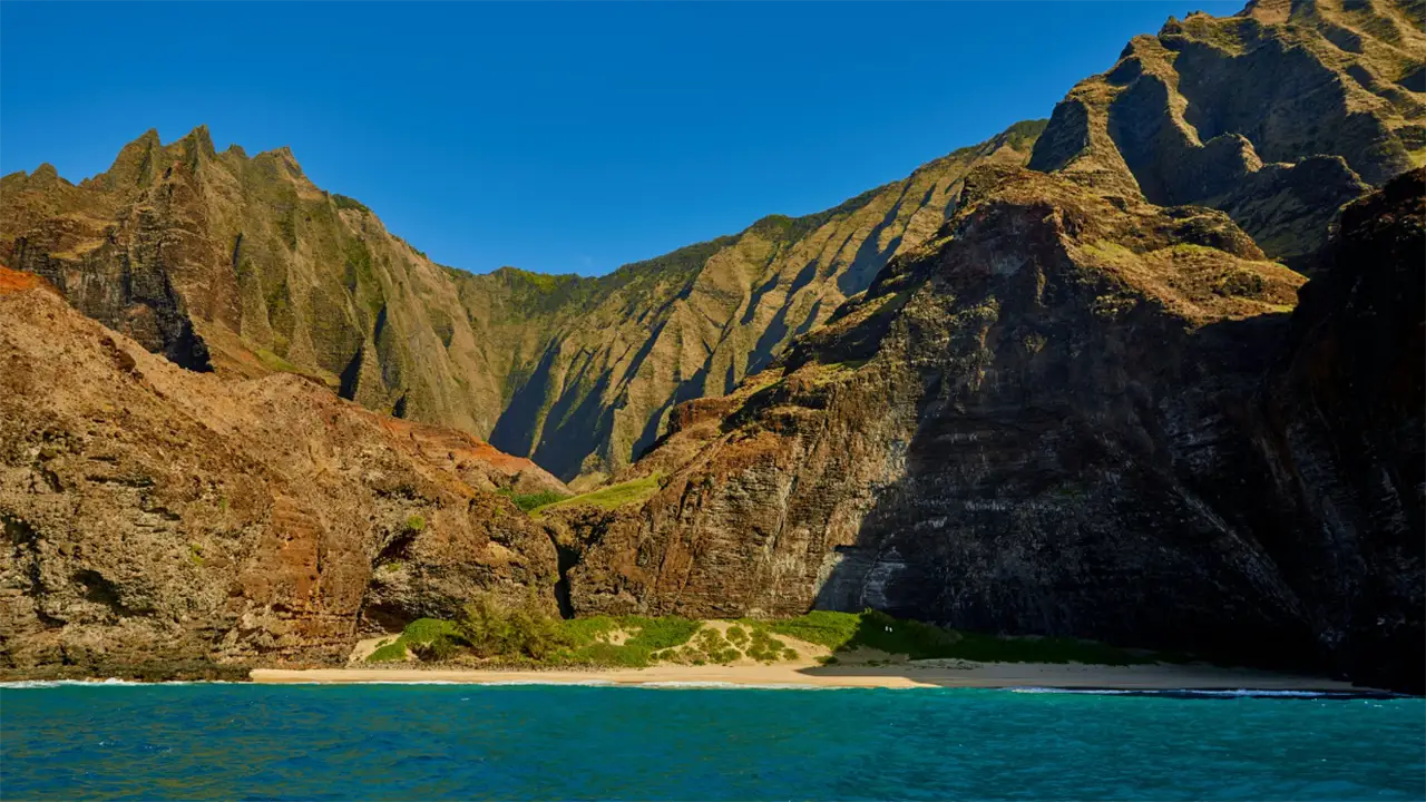 Dramatic cliffs and beach along a coastline under a clear blue sky.