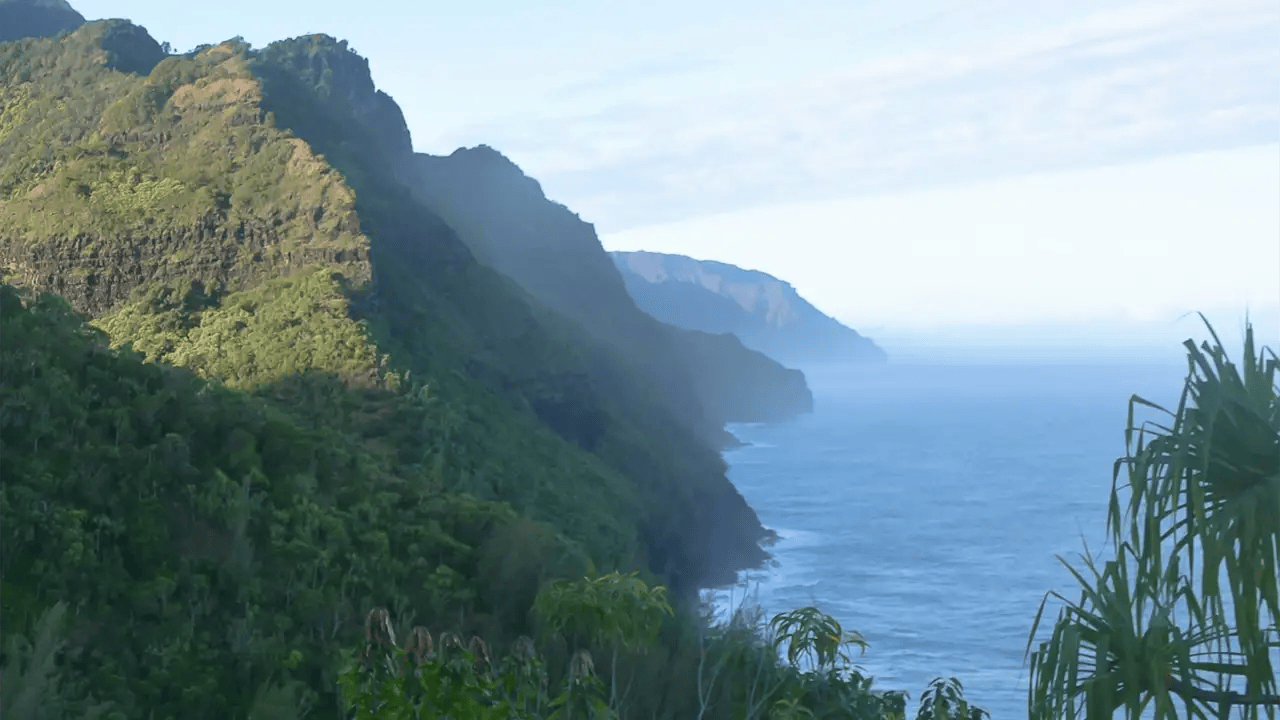 Green cliffs by the ocean under a partly cloudy sky.
